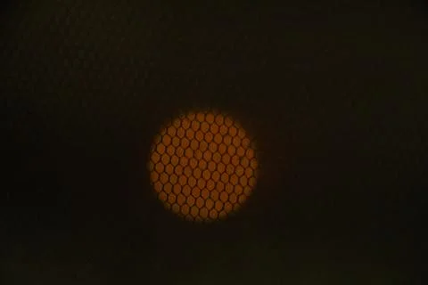 Close-up view of a glowing orange circle seen through a hexagonal mesh, likely Stock Photos