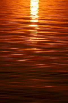 Close-up view of golden sunset light reflecting on the gentle ripples of a dark Stockfoto's