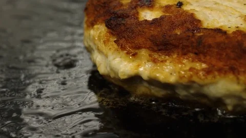 Close-up view of grilling burger cutlet, camera moves to right, bubbling oil Stock Footage 76897827