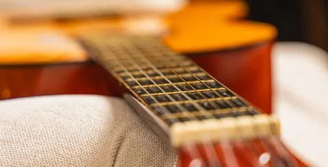 Close view of guitar resting on couch with focus on strings and body Stock Photos