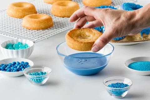 Close up view of a hand about to dip a donut into melted blue chocolate. Stock Photos
