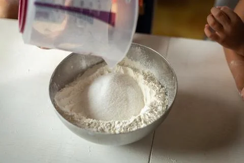 A close view of the hand of the child adding sugar to flour Stock Photos
