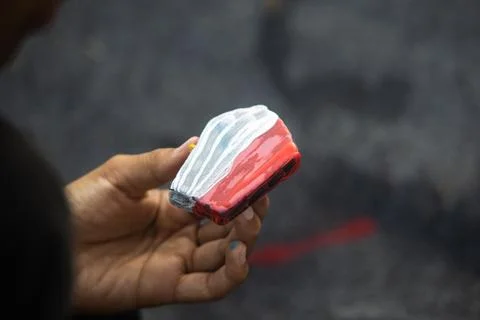 Close Up View of Hand Displaying Painted Flat Rock with Red and White Strip.. Stock Photos