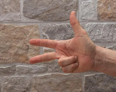 A close-up view of a hand gesturing the number three, set against a rugged .. Stock Photos