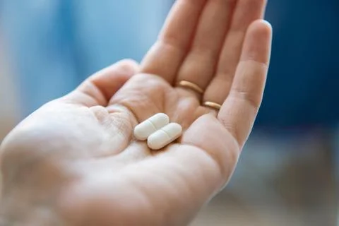 Close-up view of a hand holding two white pills in the palm above a blurry Stock Photos