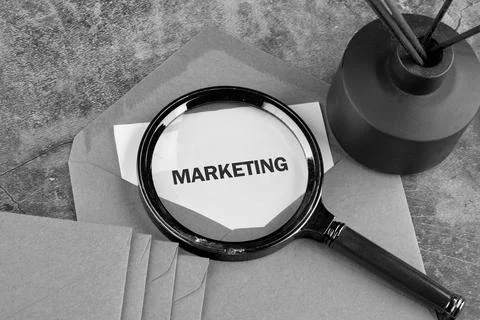 Close up view of a hand lens highlighting the word Marketing printed on white Photos