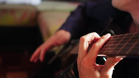 Close view of a hand playing guitar strings in a cozy room during a music practi Stock Footage 330889452