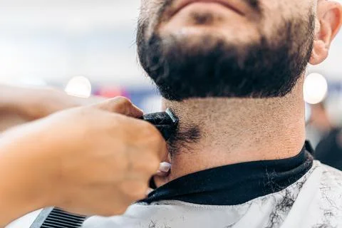 Close up view of a hand shaving a beard with an electric razor in a salon Stock Photos