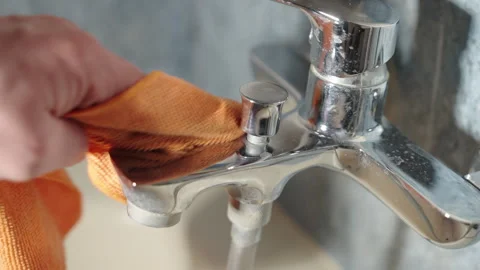 Close-Up View of Hand Wiping Chrome Bathroom Faucet with Orange Microfiber Stock Footage 329521610