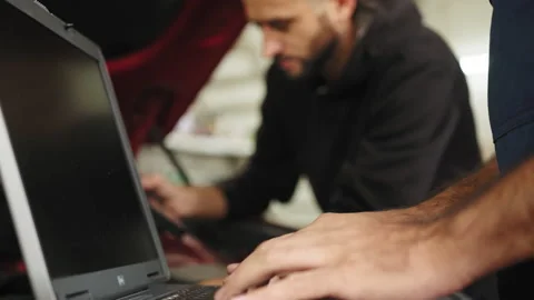 Close up view of hand of young male mechanic using laptop and his colleague with Stock Footage 233720557