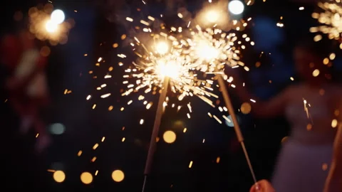 Close-up view of handheld sparklers illuminating the night with bright golden Vídeos de archivo 312509708