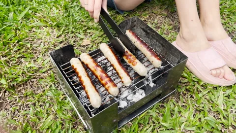 A close-up view of hands flipping browned sausages on the grill with skewers Stock Footage 281121336