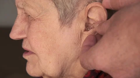 Close-up view of hands inserts hearing aid device to the elderly woman's ear 動画素材 168831576