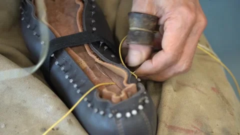 Close view of hands pulling yellow waxed thread tight while hand sewing the 動画素材 346303254