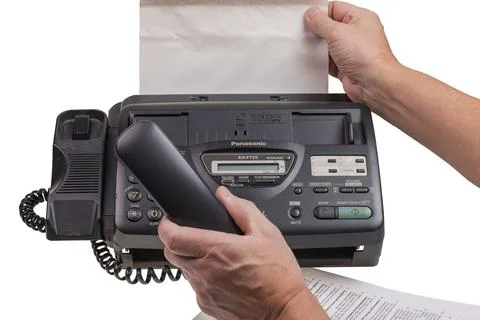 Close-up view of hands receiving printed document from Panasonic fax machine Stock Photos