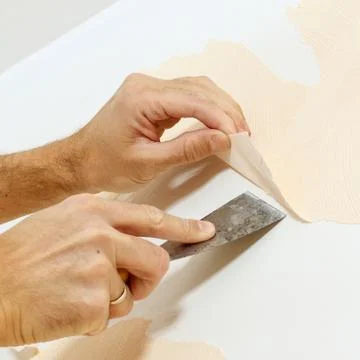 Close-up view on hands with a scraper in the process of removing wallpaper. Stock Photos