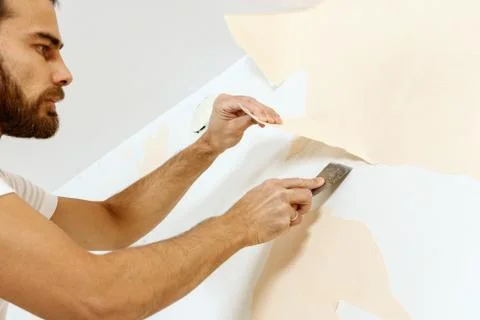 Close-up view on hands with a scraper in the process of removing wallpaper. Stock Photos