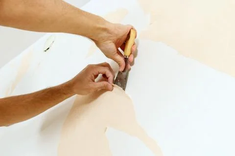 Close-up view on hands with a scraper in the process of removing wallpaper. Stock Photos