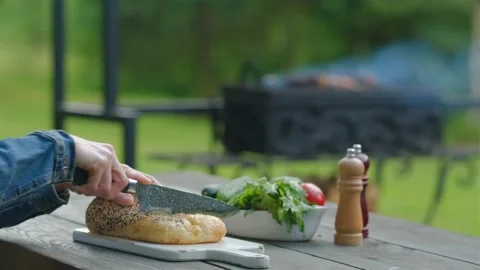 Close-up view of hands slicing fresh bread in backyard with barbecue in bac.. Stock Footage 339134999
