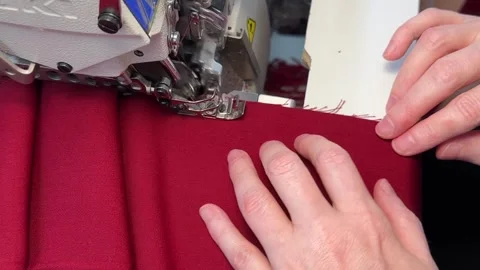 A close-up view of hands as they guide piece of red fabric through serger Stock Footage 312565622