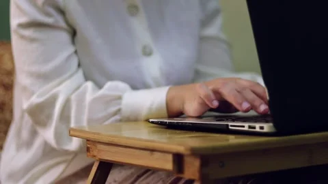 A close-up view of hands typing on a laptop placed on a wooden desk, emphasizing Video stock 313956440