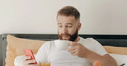 Close up view of handsome bearded man drinking coffee in bed and smiling to Stock Footage 127152405