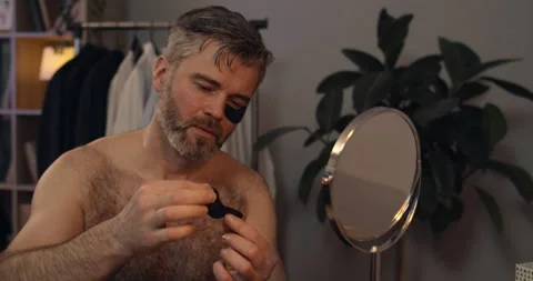 Close up view of handsome man in 40s applying black eye patches and looking in Stock Footage 136478068