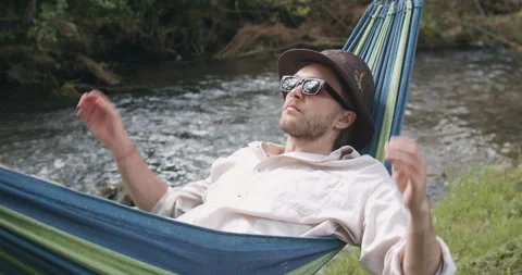 Close-Up View. Handsome man in a hat and sunglasses lying and swinging in a Stock Footage 135455989