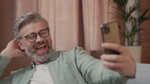 Close up view of handsome middle aged man with grey hair sitting on the sofa Vídeos de archivo 220201318
