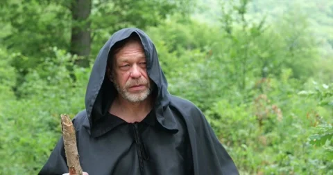 Close view of a hooded monk carrying a wooden staff while moving through a fores Stock Footage 336695326