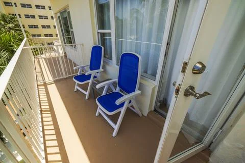 Close-up view of hotel balcony with two blue chairs near open door on sunny day. Stock Photos