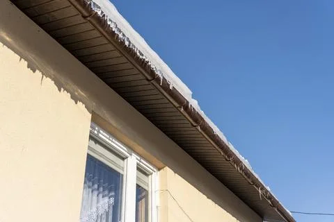 Close-up view of a house eaves with snow on the roof against a clear blue sky. Stock-Fotos