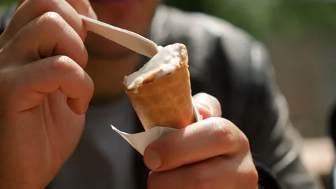 Close up view of ice cream cone, man eating ice cream with spoon on sunny bright Stock Footage 280402336