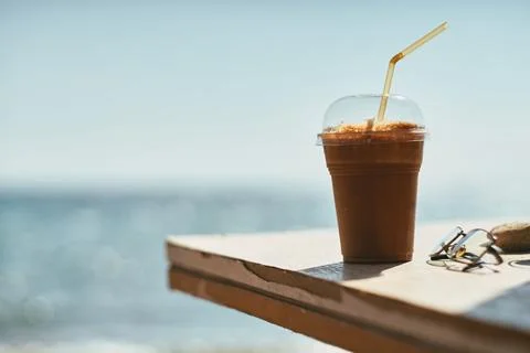 Close-up view of iced coffee in plastic cup on table by the sea Stock Photos