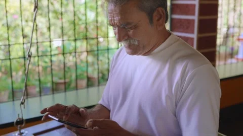 Close up view of Indian elderly man using mobile phone in rural house setting.  Stock Footage 341515326
