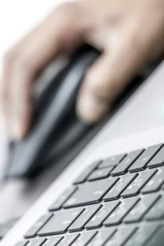 Close-up view of keyboard with hand on mouse in blurred background. Stock Photos