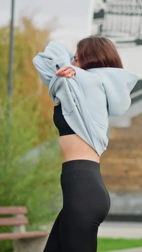 Close-up View of Lady Removing Blue Sweater in Park with Buildings and Trees Vídeos de archivo 318580359