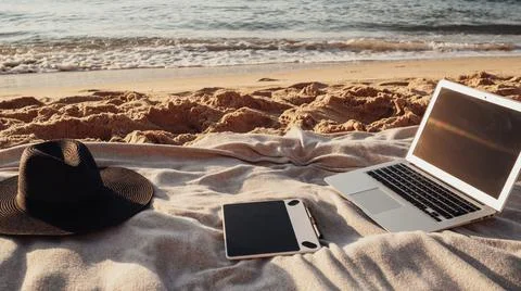 Close Up View of Laptop, Tablet and Hat Lying on the Plaid on Sandy Beach by the Stock Photos