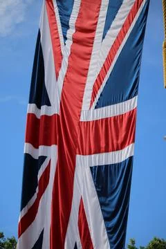 Close-up view of a large Union Jack flag hanging vertically against a blue .. Stock Photos