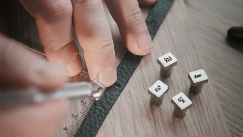 CLose up view of leather bracelet and metal tools for punching letters. Leather Stock Footage 153196029