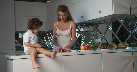 Close-up view of a little boy seated on a kitchen counter playing with tomatoes Stock Footage 123216232