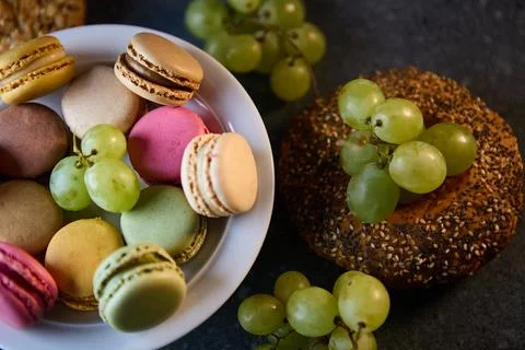 Close view of macarons beside seeded bagel and grapes on stone surface Foto stock