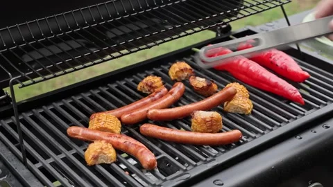 Close up view of man hand turning sausages on gas grill with roasted vegetables Stock Footage 334213298