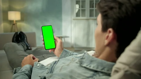 Close Up View of Man at Modern Room Lying on a Sofa Using Phone With Green Mock Stock Footage 133237027
