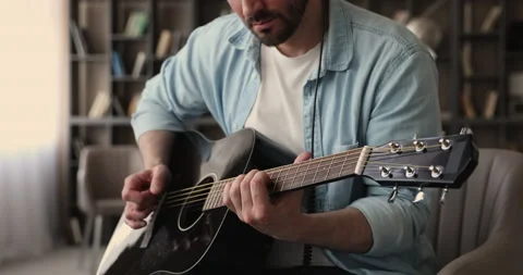 Close up view man playing acoustic guitar seated in office Stock Footage 146290214