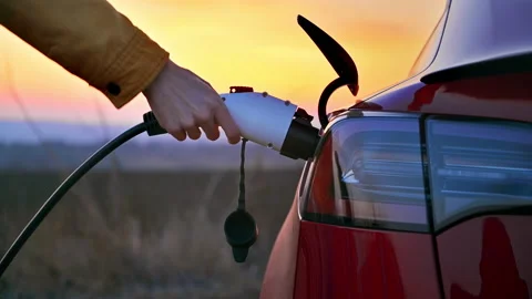 Close view of a man plugging charging cable into a parked red electric car at Video stock 235283229