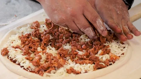 Close up view of a man preparing a pizza, placing meat on pizza dough.  스톡 동영상 137530916