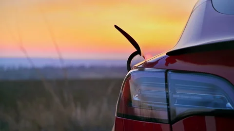 Close view of a man pulling out charging cable of a parked red electric car at Stock Footage 235283179