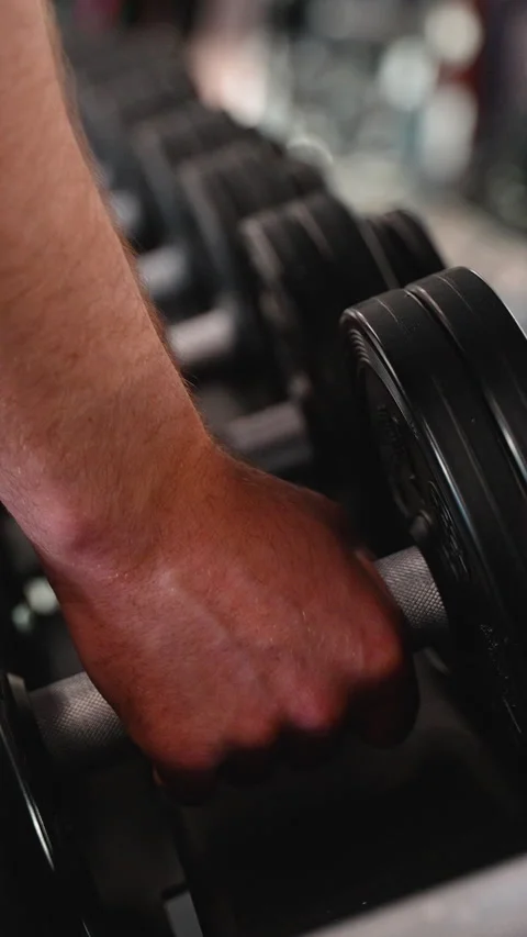 Close-up view of a man s hand grabbing a dumbbell from a weight rack in a modern Stock Footage 309070361