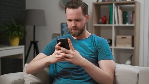Close-up view of a man scrolling the feed in an app on his mobile phone in room Stock Footage 108788178